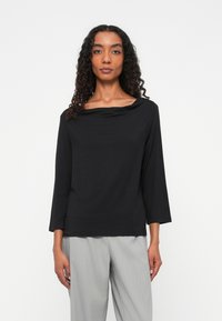 Zwarte top met lange mouwen en een brede, gedrapeerde halslijn, gemaakt van een soepele, lichte stof. Gecombineerd met lichtgrijze, gestreepte broek.
