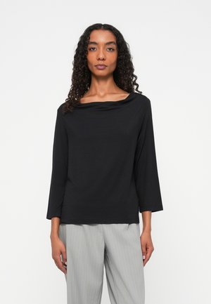 Zwarte top met lange mouwen en een brede, gedrapeerde halslijn, gemaakt van een soepele, lichte stof. Gecombineerd met lichtgrijze, gestreepte broek.