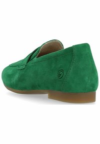 Chaussure slip-on en suede vert avec un bout arrondi, un talon bas et un logo de marque visible à l'arrière. Texture douce et éléments de design simples.