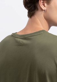 Olijfgroene crewneck t-shirt gemaakt van zacht materiaal, met een subtiel geborduurd schaarlogo op de achterkant nabij de halslijn.