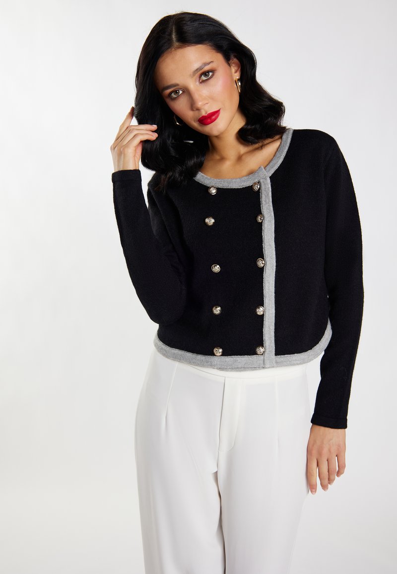 Zwart cropped cardi met zilveren knopen, lichtgrijze accenten, ronde halslijn en lange mouwen. Wollen textuur en fitted design.