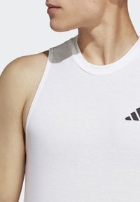 Hvid tanktop lavet af bomuld med en ribbet halsudskæring, prydet med et sort Adidas-logo på venstre brystområde og en tætsiddende pasform.