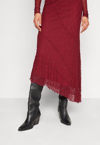 Bordeaux kanten rok met asymmetrische zoom en golvende randen, gecombineerd met zwarte leren kniehoog boots met een puntige neus en blokhak.