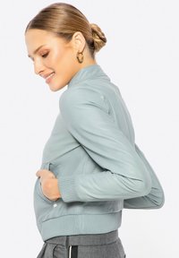 Lichtblauwe leren bomberjack met een geribbelde zoom en manchetten, voorzien van een staande kraag en zijzakken. Zachte textuur en aansluitend ontwerp.