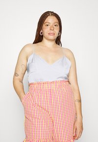Camisola de cetim cinza claro com alças finas, combinada com calções de gingham rosa e amarelo com bainha franzida e bolsos laterais.