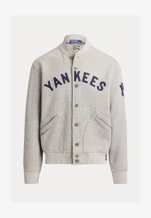 Lys grå varsityjakke med knappelukking, med "YANKEES" i marineblått foran, skrålommer og New York Yankees-logo på venstre erme.