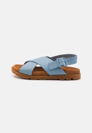 Blå läder-sandal med korsremmar som har en fotbädd i brun mocka och en robust gummisula. Spänne vid vristen för en säker passform.