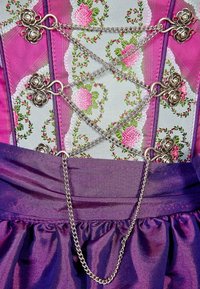 Vêtement traditionnel avec un corsage à motifs floraux orné de broderies roses et vertes, accents en chaîne argentée, et une jupe violette fluide.