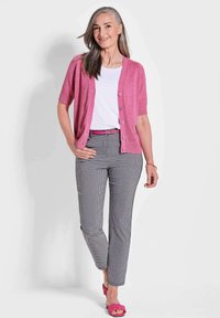 Rosa Kurzarm-Cardigan, weißes T-Shirt, schwarz-weiße karierte Hose und rosa Sandalen. Glatte Texturen und kontrastierende Farben.