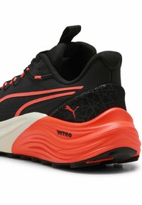 Scarpa sportiva nera con accenti rossi, tomaia in mesh testurizzato, colletto imbottito e una suola spessa e ondulata arancione etichettata "NITRO".