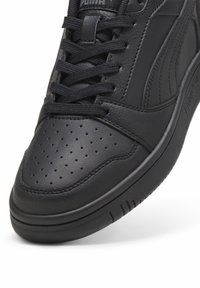 Basket en cuir noir avec une boîte à orteils perforée, lacets plats noirs et semelle texturée. Présente un logo discret sur la languette et le côté.