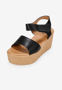 Sandales compensées en cuir noir avec deux larges brides, une semelle intérieure souple beige et une semelle plateforme texturée beige. Comprend une bride de cheville ajustable.