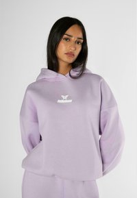 Felpa leggera viola con cappuccio, caratterizzata da una grande tasca a scomparsa frontale, vestibilità oversized e un piccolo logo bianco del marchio sul petto. Tessuto morbido.