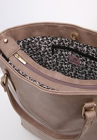 Bolso de mano de imitación de cuero en color tostado con un acento de hardware dorado. El interior presenta un patrón floral en blanco y negro y un bolsillo con cremallera.