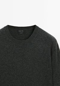 Maglione in cashmere grigio scuro con scollo a girocollo a coste. Presenta una texture liscia e un leggero luccichio. Etichetta visibile all'interno del colletto.