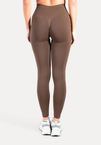 Brune leggings med høj talje lavet af strækbart stof, med tekstureret taljebånd og glatte, tætsiddende ben, kombineret med hvide sportssko.