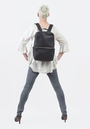 Zaino in pelle nera con spallacci regolabili, doppie tasche con zip e superficie texturizzata. Design minimalista con una silhouette elegante.