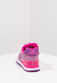 Rosa och lila New Balance-sneakers sedd från baksidan på en vit yta med en enkel ljusgrå bakgrund.