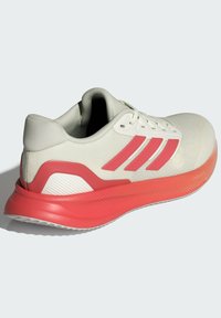 Lekkie buty sportowe z kremową siateczką, różowymi akcentami, zaokrąglonym noskiem i teksturowaną czerwoną podeszwą środkową dla amortyzacji i wsparcia.