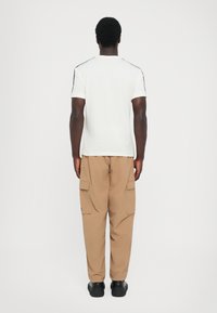 White cotton t-shirt with black shoulder accents, paired with tan cargo pants featuring side pockets and a relaxed fit. Black footwear.
