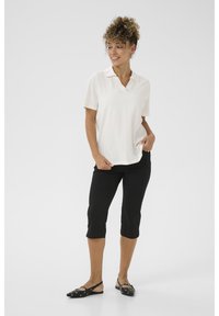 Wit korte mouwen polo met V-hals, gecombineerd met zwarte knielange capri-broeken en platte zwarte schoenen met zilveren accenten.