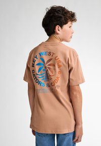Camiseta de manga corta en tono marrón con un diseño colorido de palmera y texto en la parte trasera. Material de algodón con un corte relajado. Detalles en azul y naranja.