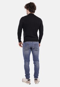 Maglione nero a maglia, jeans slim-fit blu e sneakers chiare. Il maglione ha un collo alto e maniche lunghe, con una texture liscia.
