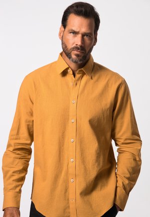 Camisa de manga larga color mostaza con cuello abotonado, fabricada en un tejido texturizado, con botones en la parte delantera y un dobladillo curvado.