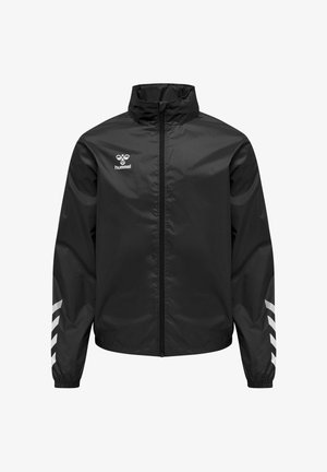 Chaqueta cortavientos negra con cremallera, cuello alto, puños elásticos, rayas blancas en forma de chevrón en las mangas y logotipo blanco de hummel en el pecho izquierdo.