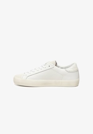 Baskets blanches en cuir avec une semelle en caoutchouc plate, présentant une texture lisse, un design à lacets et un accent à motifs sur le talon.