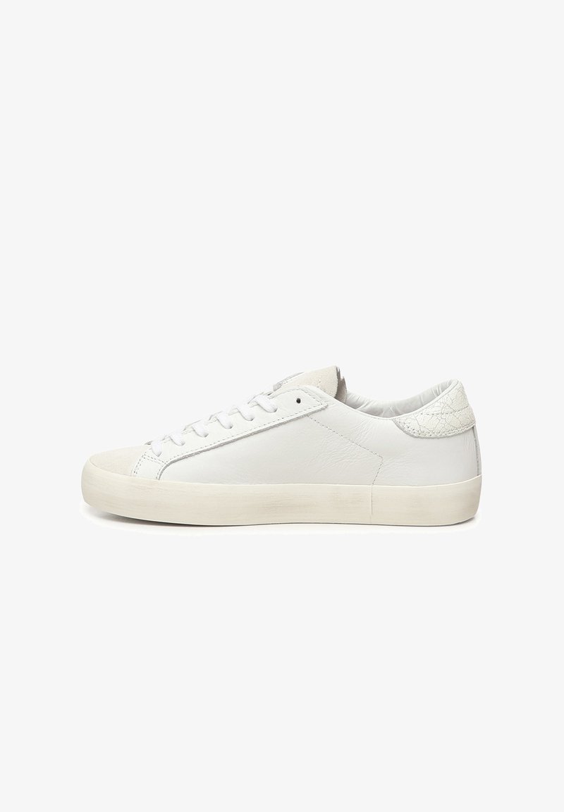 Sneaker bianchi in pelle con suola piatta in gomma, caratterizzati da una texture liscia, design con lacci e un accento decorativo sulla parte posteriore.