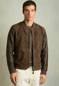 Jachetă bomber din suede maro cu mâneci din piele, guler cu arici și închidere cu fermoar; prezintă o țesătură texturată și un design ajustat.
