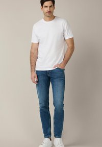 Biała bawełniana koszulka i niebieskie dżinsy o dopasowanym kroju, w połączeniu z białymi sneakersami. Prosty fason bez widocznych wzorów czy logo.