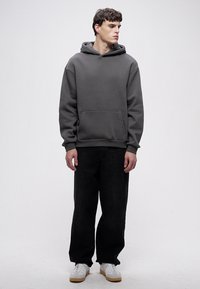 Tamnosiva majica s kapuljačom s prednjim džepom, rebrastim manšetama i rubom. Uparena s crnim širokim trapericama i bijelim tenisicama. Čist, minimalistički dizajn.