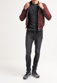 Bordový bomber s zipem přes tmavě šedé henley tričko, v kombinaci s černými skinny džínami a vzorovanými teniskami. Obsahuje přední zip a detaily na knoflících.