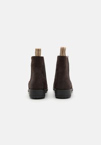 Botas Chelsea de ante marrón con paneles laterales elásticos, suela de goma negra plana y tiradores en tono beige claro con el logotipo de la marca.