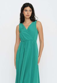 Abito avvolgente teal realizzato in un tessuto liscio; presenta una scollatura a V profonda, design senza maniche e vita arricciata, che si allarga in una gonna ampia.