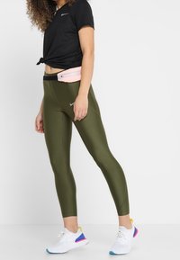 Leggings verde oliva de cintura alta, camiseta negra de manga corta y zapatillas deportivas blancas con acentos multicolores. Incluye un pouch rosa para la cintura.