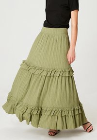 Jupe maxi verte à volants, fabriquée en tissu texturé, présentant des accents froncés le long de l'ourlet et une taille ajustée, stylisée avec un haut noir.