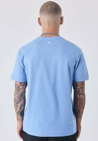 Camiseta de manga corta azul claro hecha de una tela suave, con un pequeño detalle de estrella blanca en la parte trasera y un dobladillo recto.