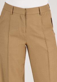 Beige op maat gemaakte broek met een rechte snit, voorzien van een flat front en twee zijzakken. Gemaakt van een gladde, lichte stof.
