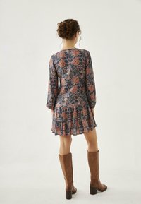 Vestido de estampado floral en azul oscuro, con mangas largas, dobladillo con volantes y tejido liviano. Llevado con botas marrones hasta la rodilla.