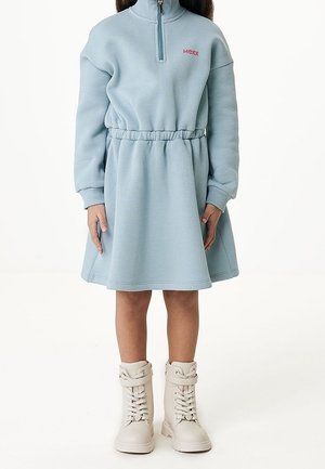 Hellblaues Sweatshirtkleid mit Stehkragen und halbem Reißverschluss, elastischer Taille und langen Ärmeln. Kombiniert mit beigen Schnürstiefeln.