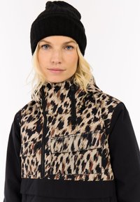 Leichte, gemusterte Jacke mit braunen und schwarzen Akzenten, ausgestattet mit einem hohen Kragen, Reißverschlusstaschen und einem einfarbigen schwarzen Unterteil. Schwarze Strickmütze.