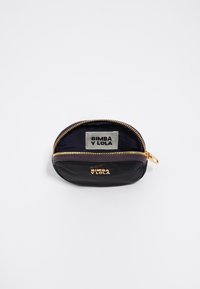 Funda negra con cremallera hecha de material suave, con una cremallera dorada y detalle del logo. En el interior presenta una etiqueta gris con el nombre de la marca.
