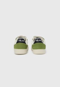 Αθλητικά παπούτσια με πράσινο σουέντ και λευκό δέρμα, με μαύρες υφασμάτινες λεπτομέρειες και λογότυπο στη φτέρνα. Στρογγυλεμένη, επίπεδη σόλα.