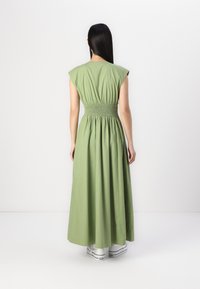 Abito senza maniche, lungo fino al pavimento, in cotone verde oliva con vita arricciata e vestibilità rilassata, abbinato a sneakers bianche basse.