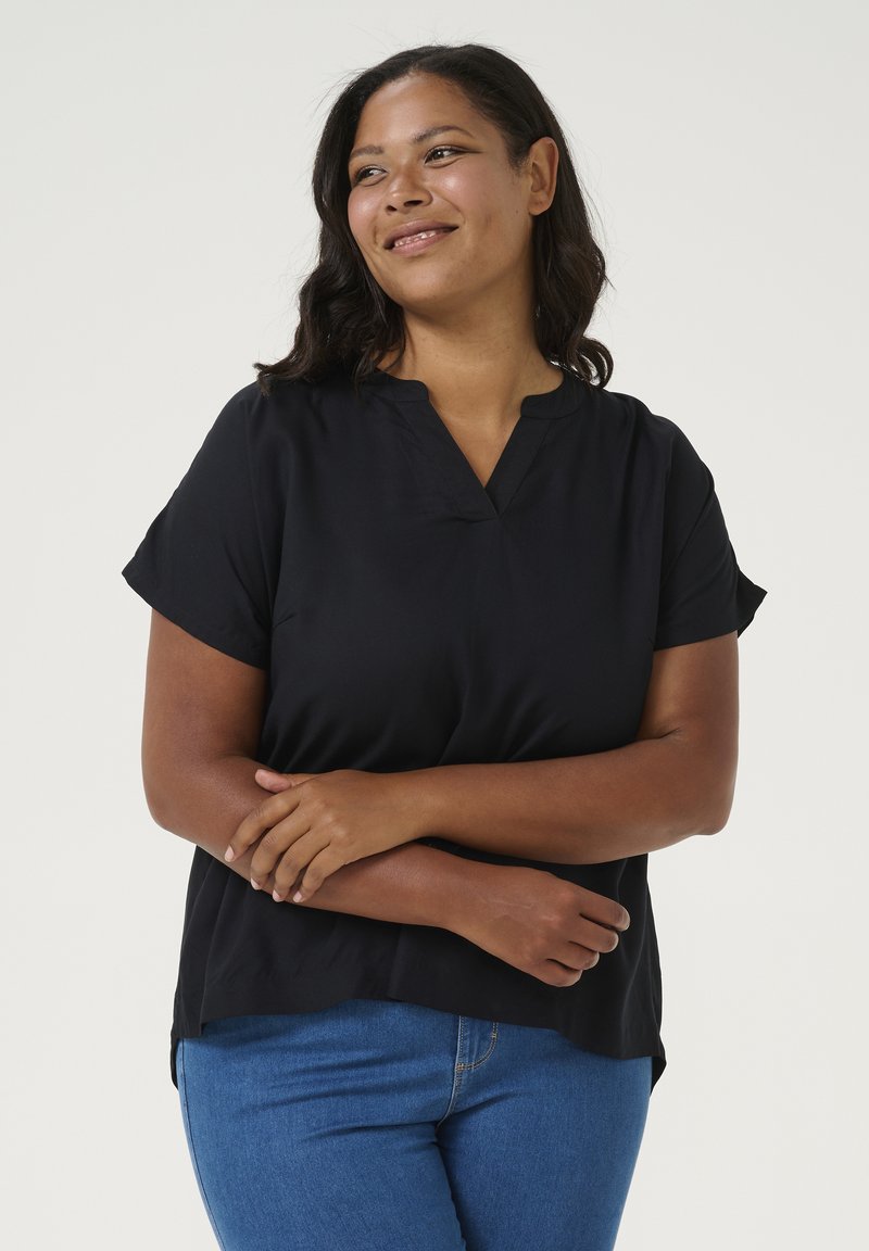 Haut noir à manches courtes avec un col en V, coupe décontractée et texture douce. Associé à un jean bleu ajusté, à ourlet incurvé.
