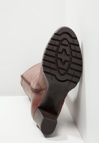 Stivale alla caviglia in pelle marrone con superficie effetto texture e cerniera laterale, con suola in gomma nera dotata di un motivo battistrada e tacco a blocco.