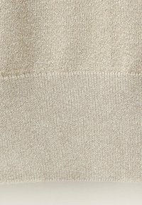 Gros plan d'un tissu tricoté beige montrant deux motifs de points avec une couture horizontale divisant un tricot côtelé plus serré d'un tricot plus lâche au-dessus.